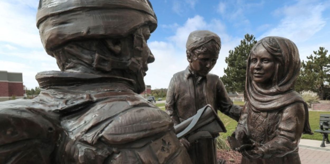 Statue of a soldier kneeling down in front of a boy and a girl. The girl is holding a butterfly in her hand.